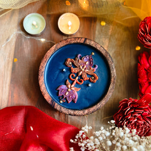 Decorative soy wax candle with multi coloured Autumn themed floral design on a blue surface, in a wooden bowl. Handcrafted artisanal festive candle